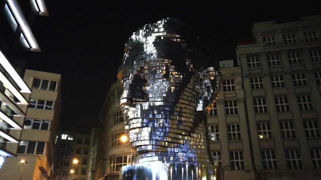 Picture of the Franz Kafka statue in Prague at night with light reflecting of the stainless steel statue